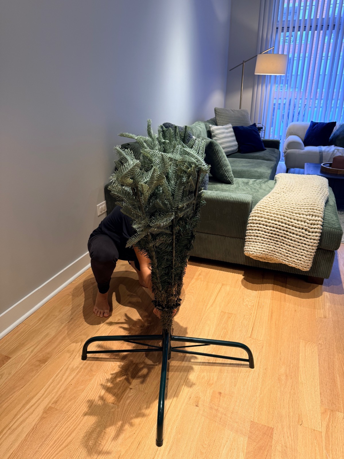 A person assembles the metal base of a firecracker lights Christmas tree in a living room.