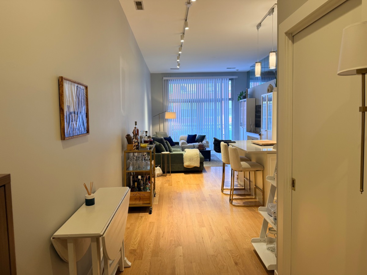 View through a hallway into an apartment with a bar cart, kitchen island, and a sofa draped in firecracker lights.