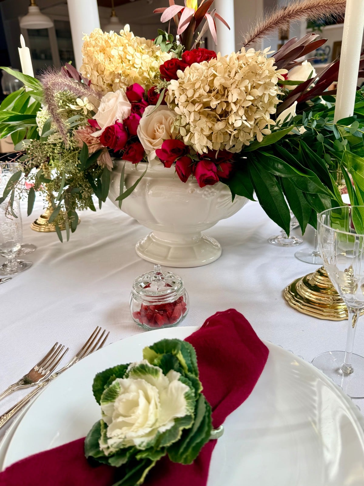 A white floral centerpiece, red napkins, and a cabbage leaf garnish on a plate for small house thanksgiving dining.