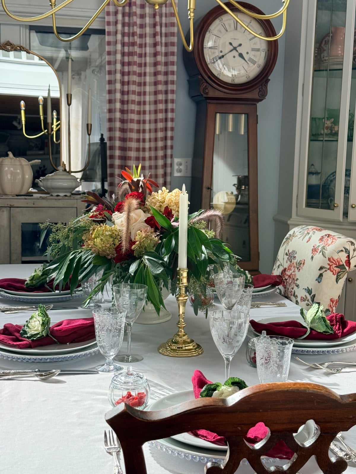 A Thanksgiving table set with a floral centerpiece, white candles, red napkins, and crystal glassware.
