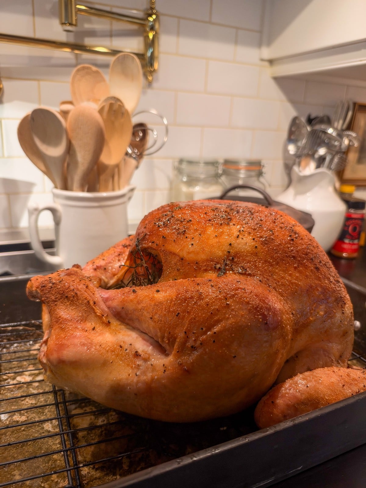 A golden-brown roasted turkey on a wire rack for a small house Thanksgiving, with kitchen utensils in the background.