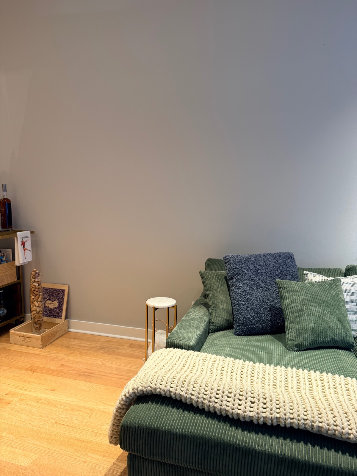 A green corduroy sectional with a knit blanket, side table, wine corks, and firecracker lights near a Christmas tree.
