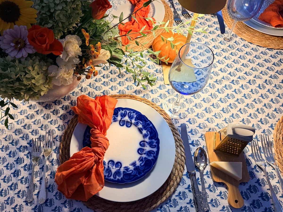 Perfect setup to host a fall dinner party—blue and white plates, orange napkins, flowers, pumpkin, and wine glasses.