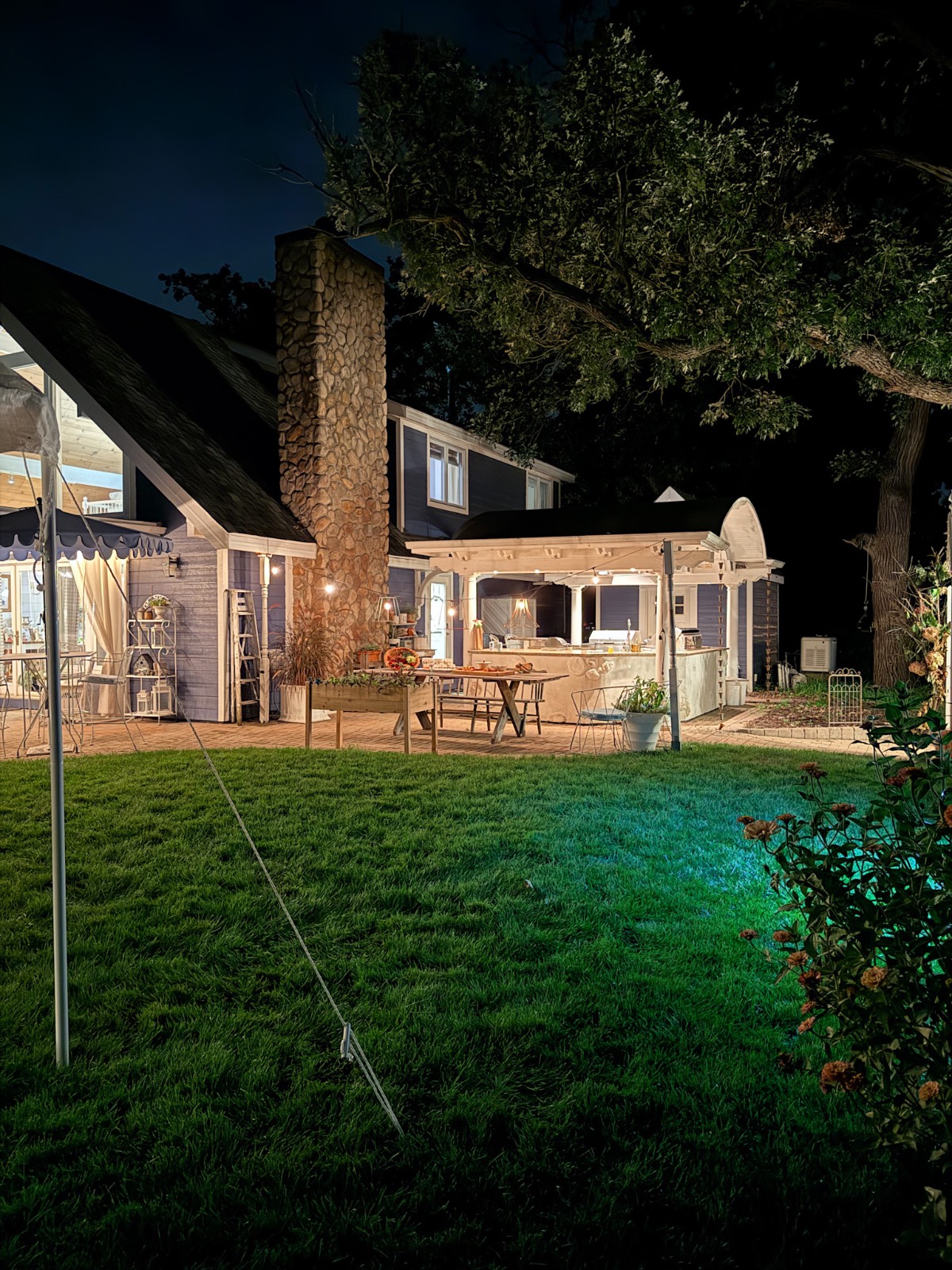 A cozy house at night with warm lights, perfect for an outdoor fall dinner party on the lush green lawn.