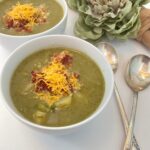 Two bowls of green vegetable soup topped with cheddar and bacon for your shopping list, served with two spoons.