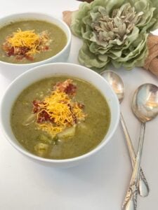 Two bowls of green vegetable soup topped with cheddar and bacon for your shopping list, served with two spoons.