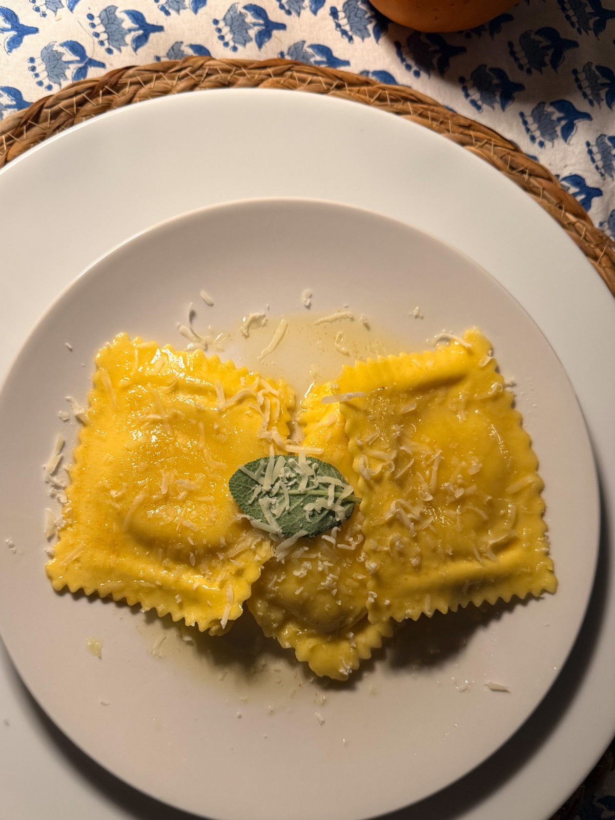 Three ravioli with grated cheese and a sage leaf, perfect for your outdoor fall dinner party, on a woven placemat.