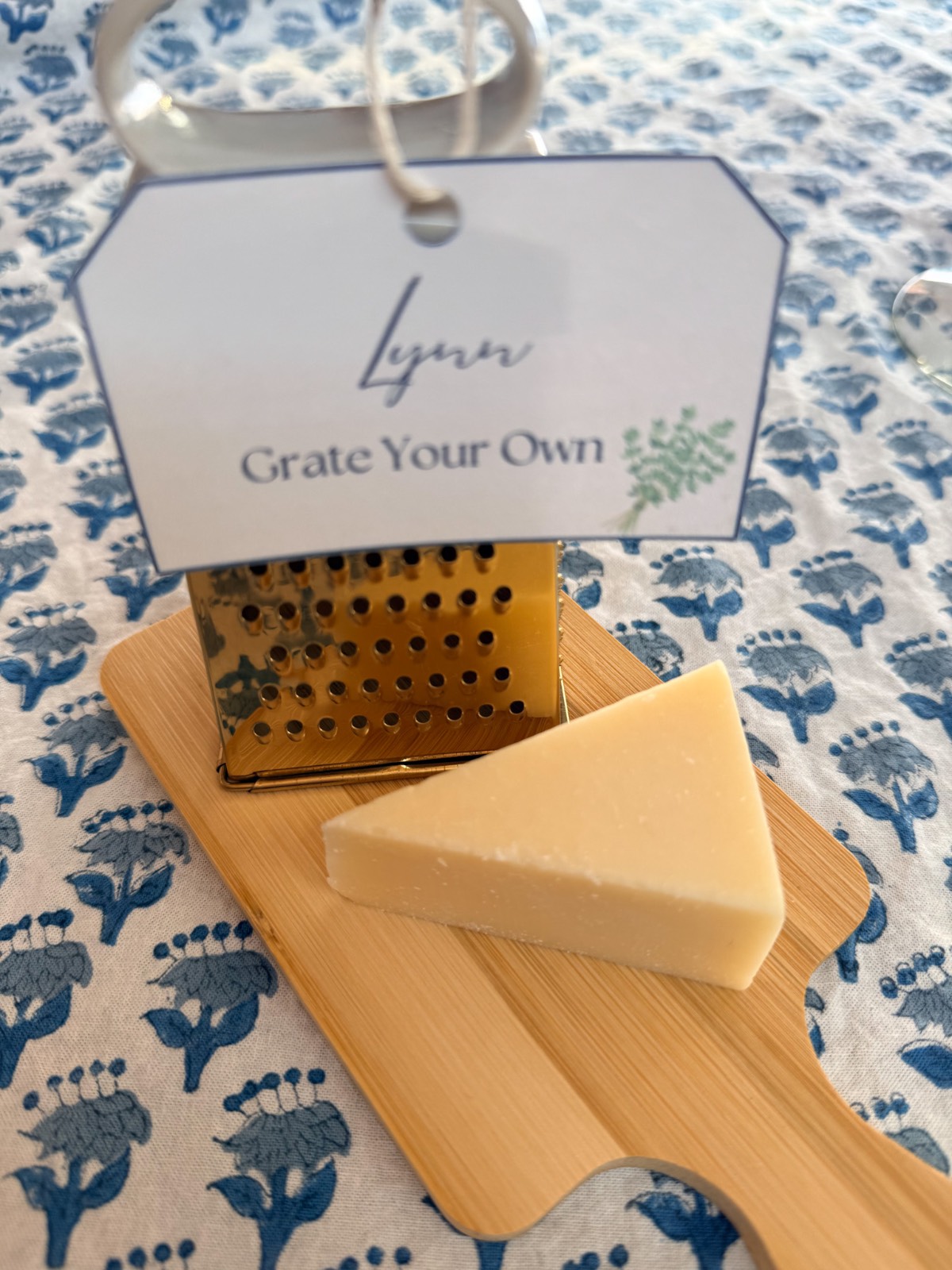A cheese grater and wedge on a wooden board at a fall dinner party with a tag: “Lynn, Grate Your Own.”.