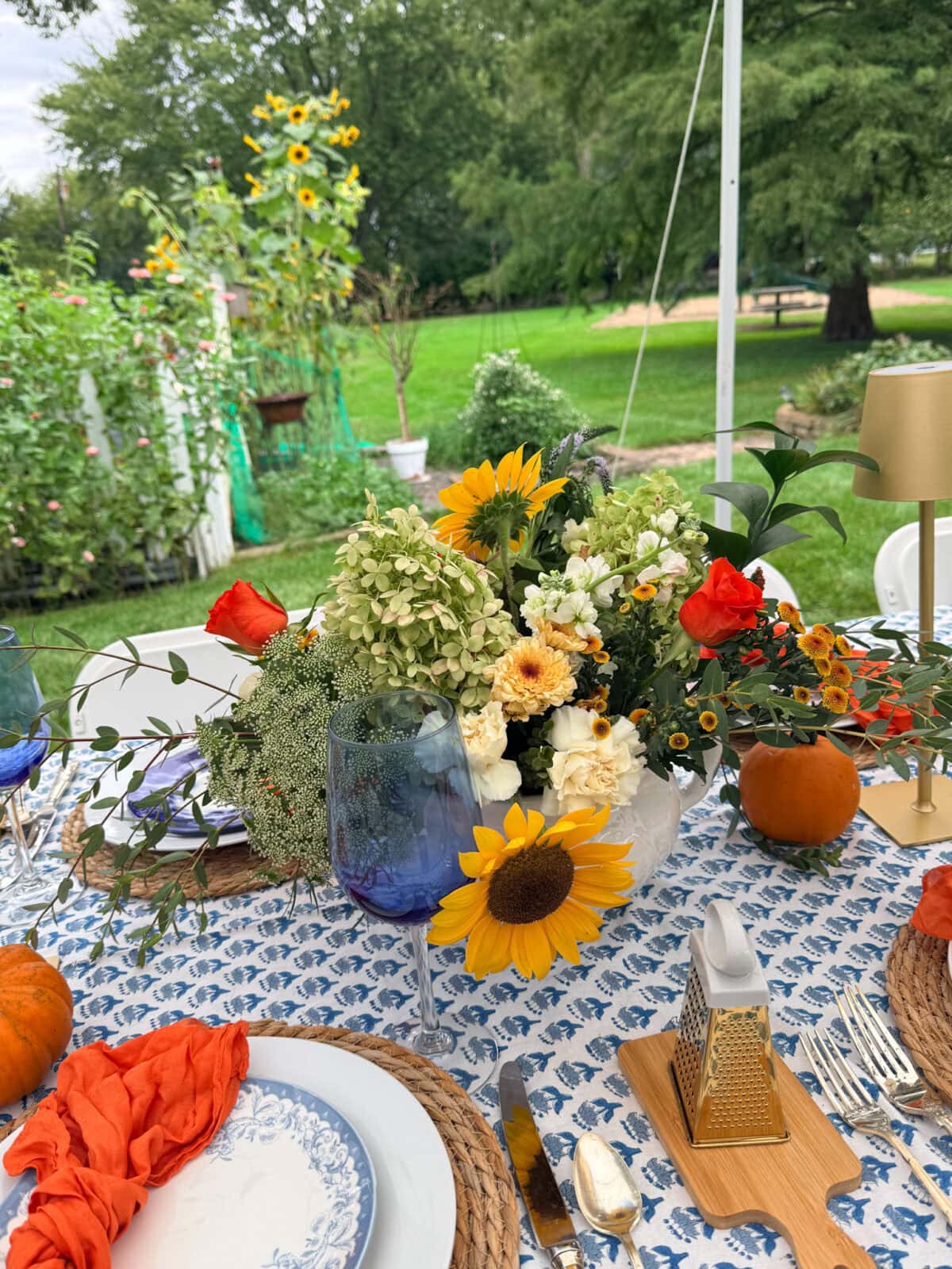 Outdoor table set for 16, perfect to host an outdoor fall dinner party with blue-white plates and a floral centerpiece.
