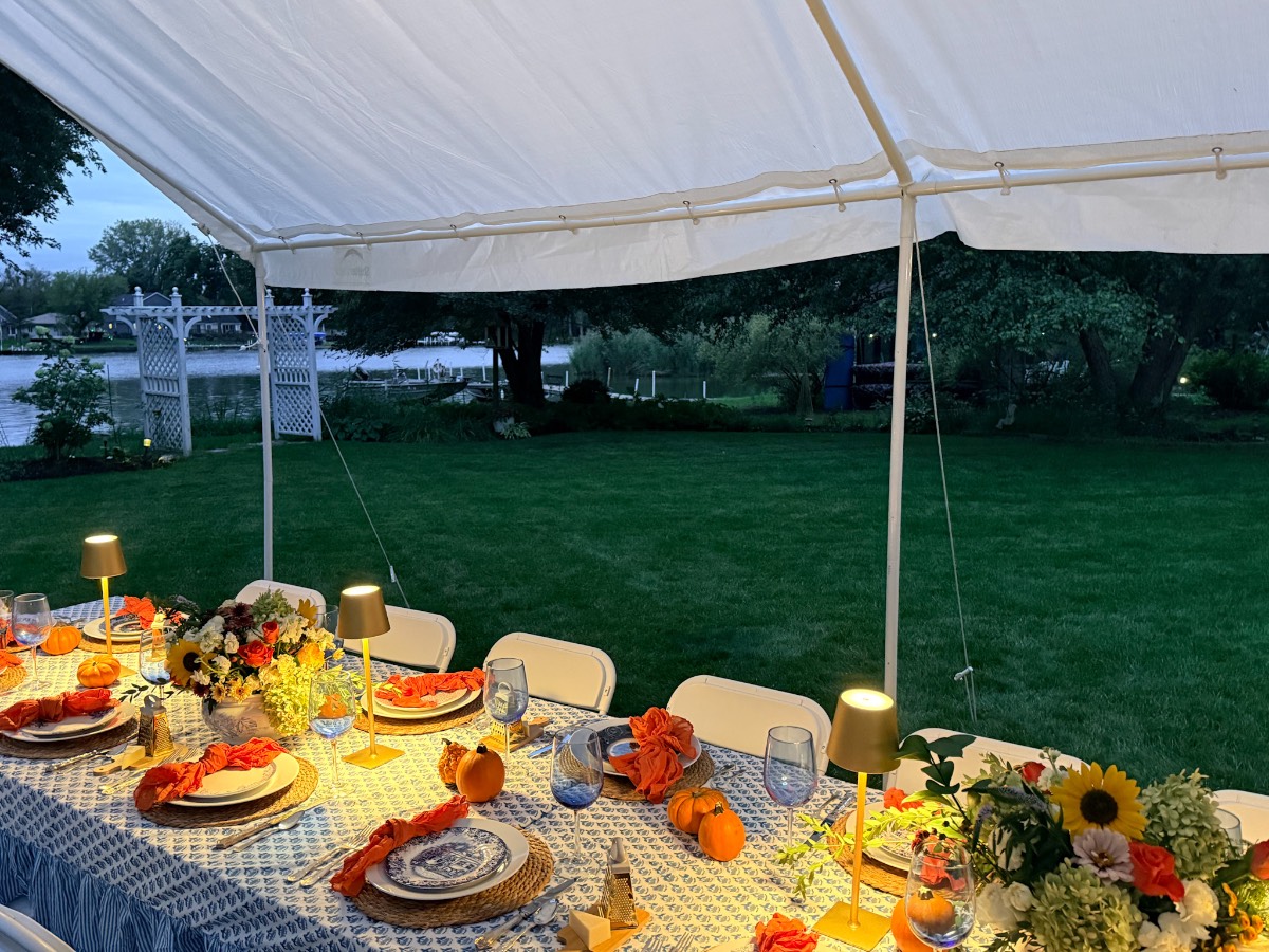 Host a magical outdoor dinner party at a long table with flowers and lights, overlooking a green lawn by the water.