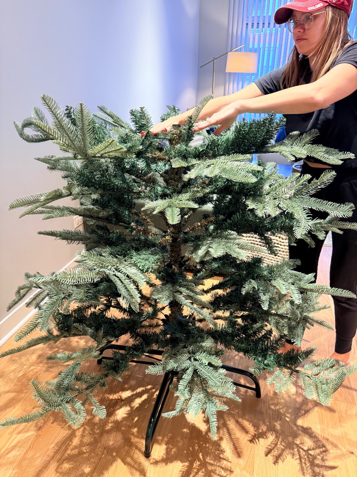 A person in a baseball cap assembles a synthetic Christmas tree adorned with firecracker lights.